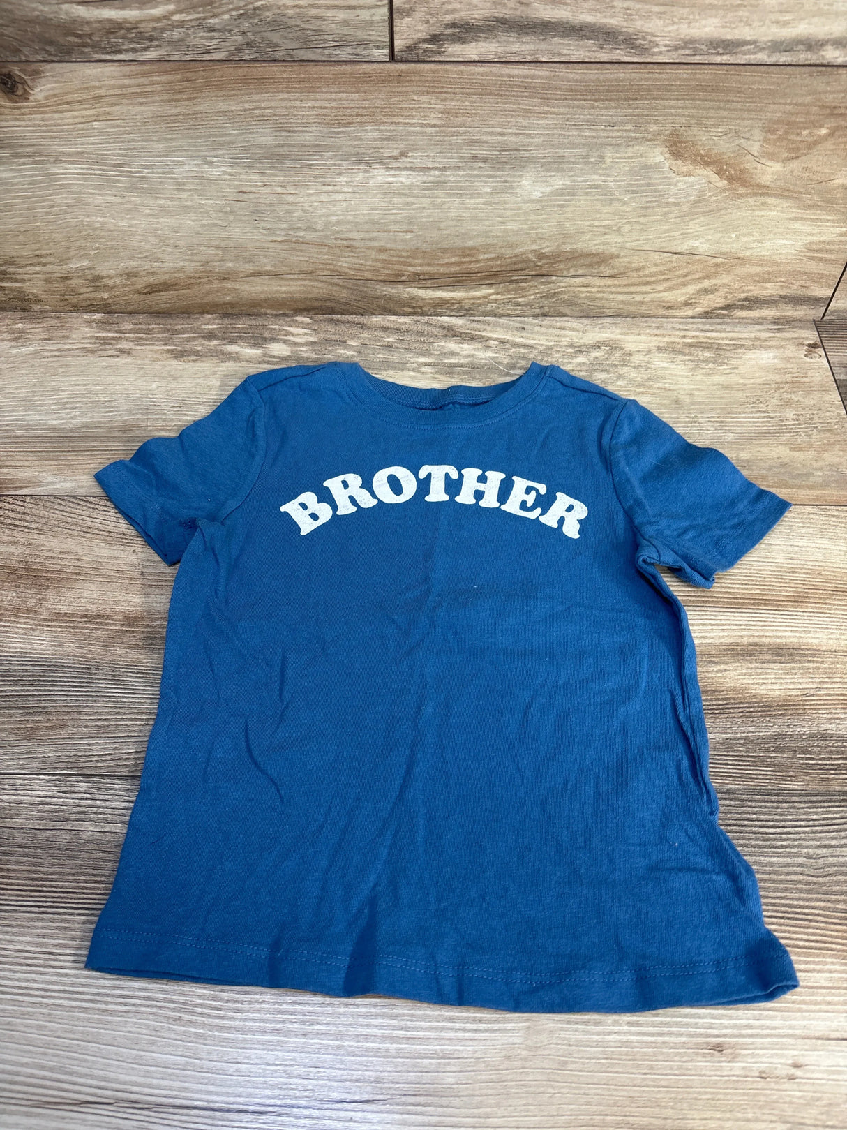 Blue kids t-shirt with white 'BROTHER' text on wood floor, gently used children's clothing