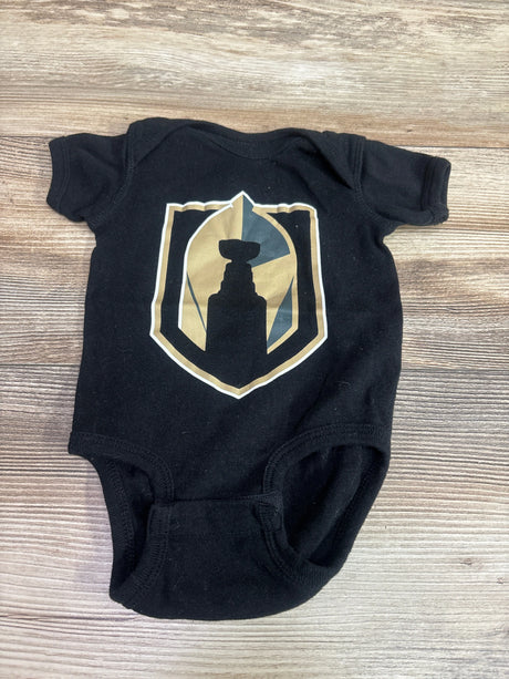 Front view of black Golden Knights Stanley Cup baby bodysuit, size 6 months, showcasing shield crest on wood-grain background