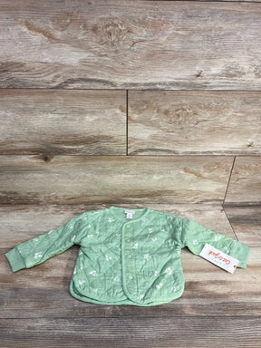 Light green quilted baby jacket with white floral patterns and snap buttons on wooden floor
