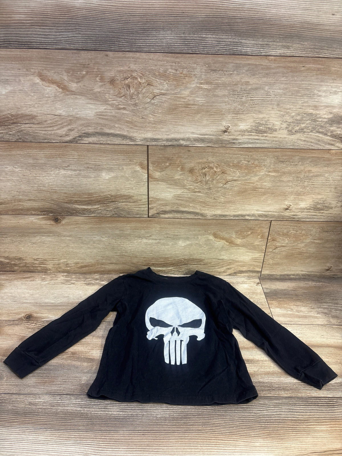 Front view of a black Marvel The Punisher long sleeve shirt showcasing a white skull graphic on a wood-look floor