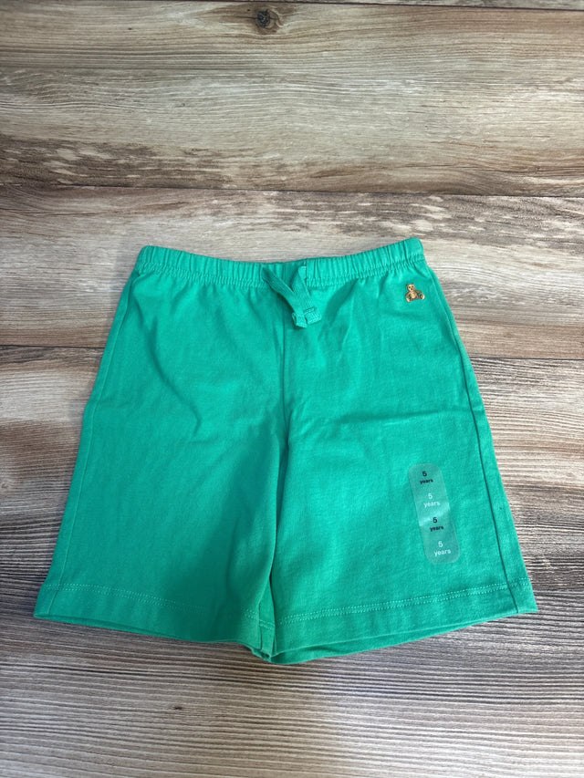 Green kids shorts with drawstring waist, teddy bear logo, size 5 years, laid on wood floor