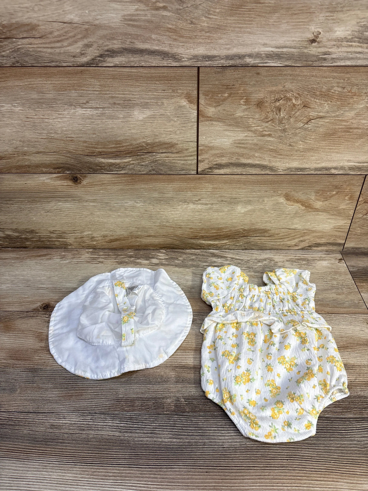 Flat lay of white newborn bubble romper and matching sun hat showcasing smocked bodice and yellow floral pattern on wood background