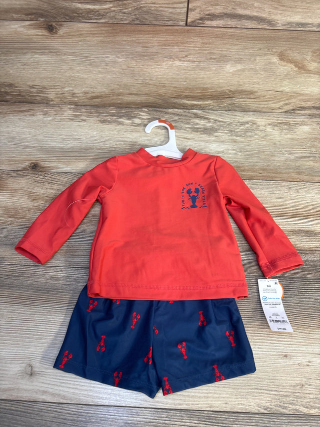 Red long sleeve baby rash guard and navy swim shorts with lobster print on wood floor.