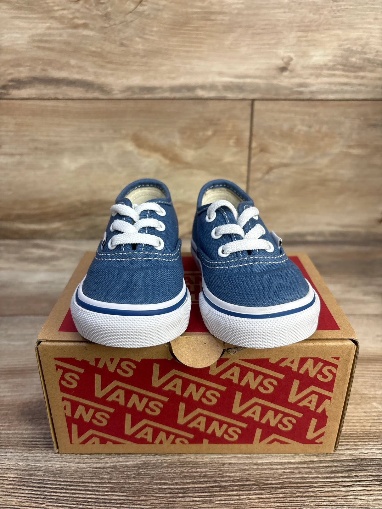 Front view of Vans Authentic low-top toddler sneakers in navy showing white laces and white rubber soles on a Vans box on a wood surface