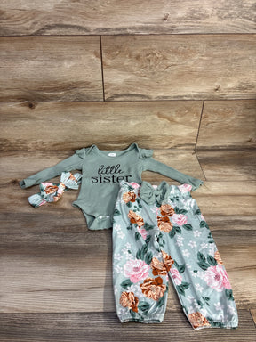 Flat lay of green 4-piece baby outfit: ribbed onesie reading little sister, floral elastic-waist pants, matching headband