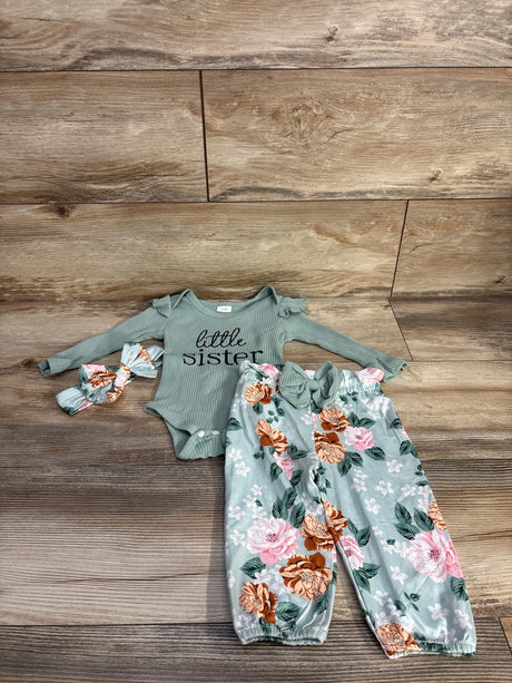 Flat lay of green 4-piece baby outfit: ribbed onesie reading little sister, floral elastic-waist pants, matching headband