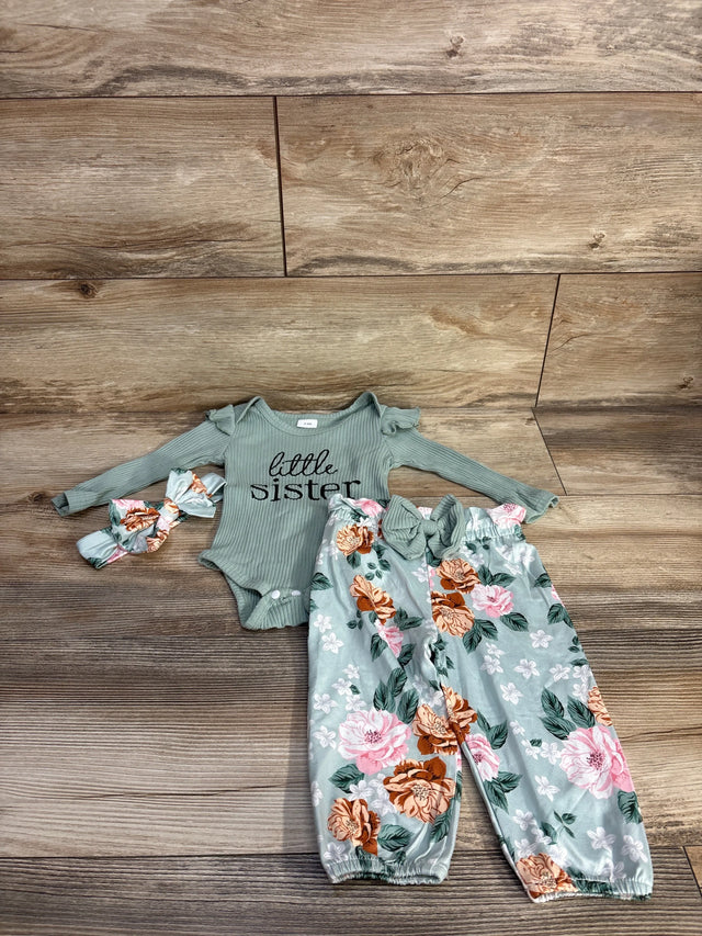 Flat lay of green 4-piece baby outfit: ribbed onesie reading little sister, floral elastic-waist pants, matching headband