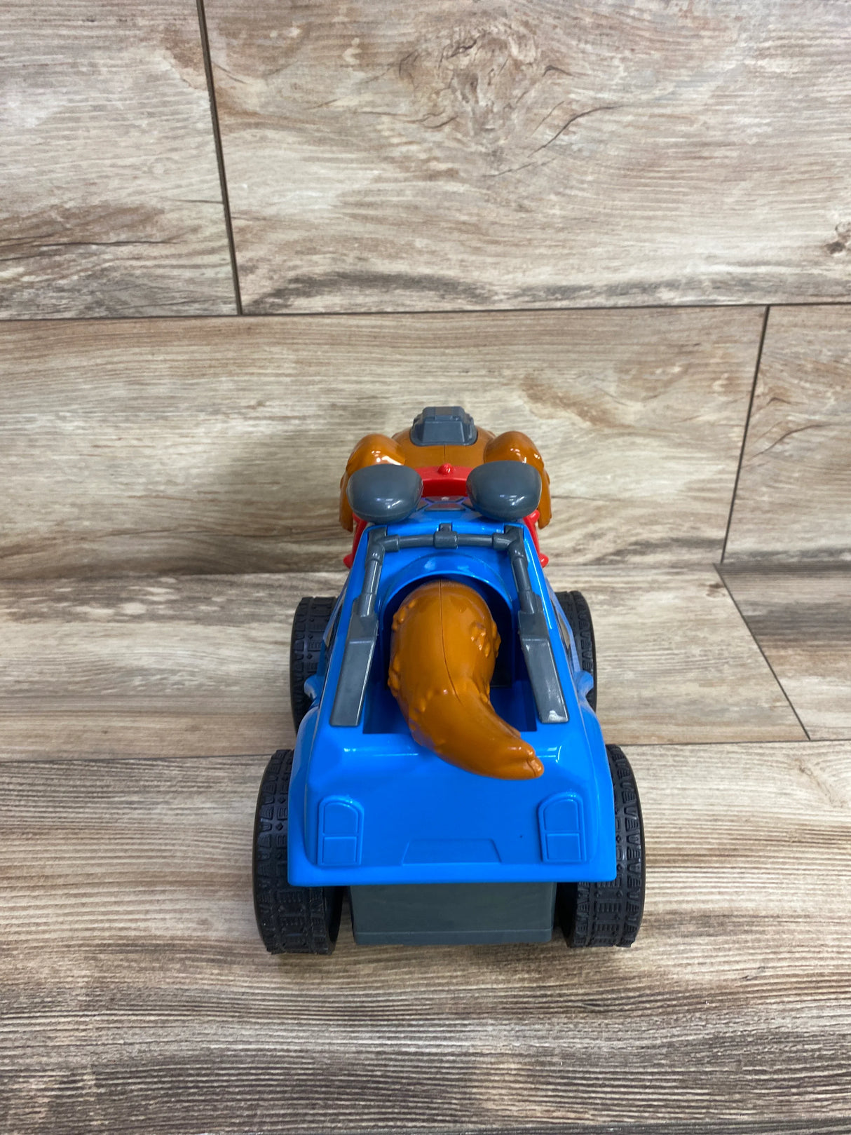 Kids toy vehicle with blue body, black wheels, and brown dog figure tail on wooden floor