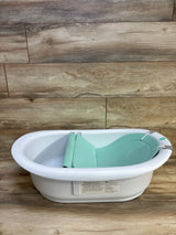 Angled view of Frida Baby 4-in-1 Grow-With-Me Bath Tub showing mint infant insert and white tub on wood background