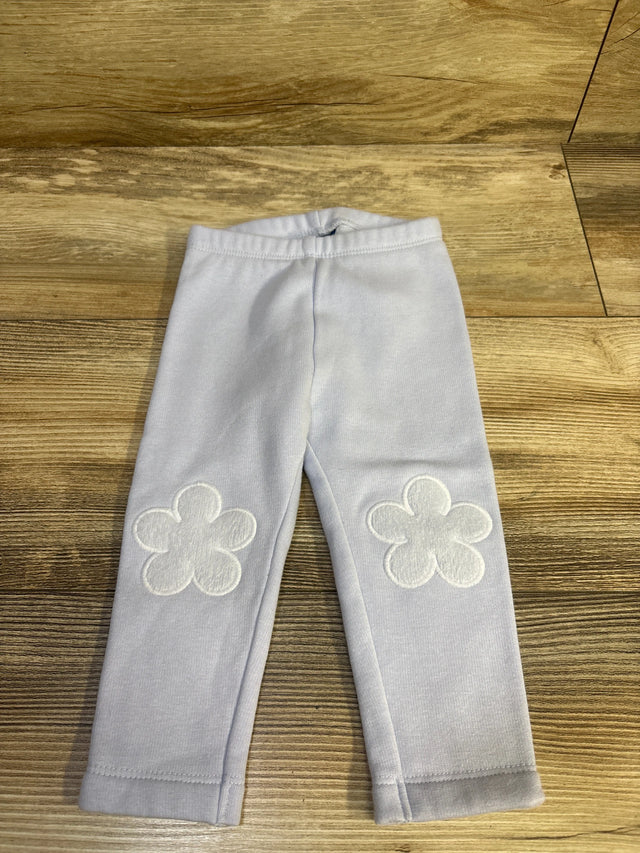 Front view of Old Navy blue leggings in size 12 to 18 months with flower patches on the knees, laid flat on a wood grain surface