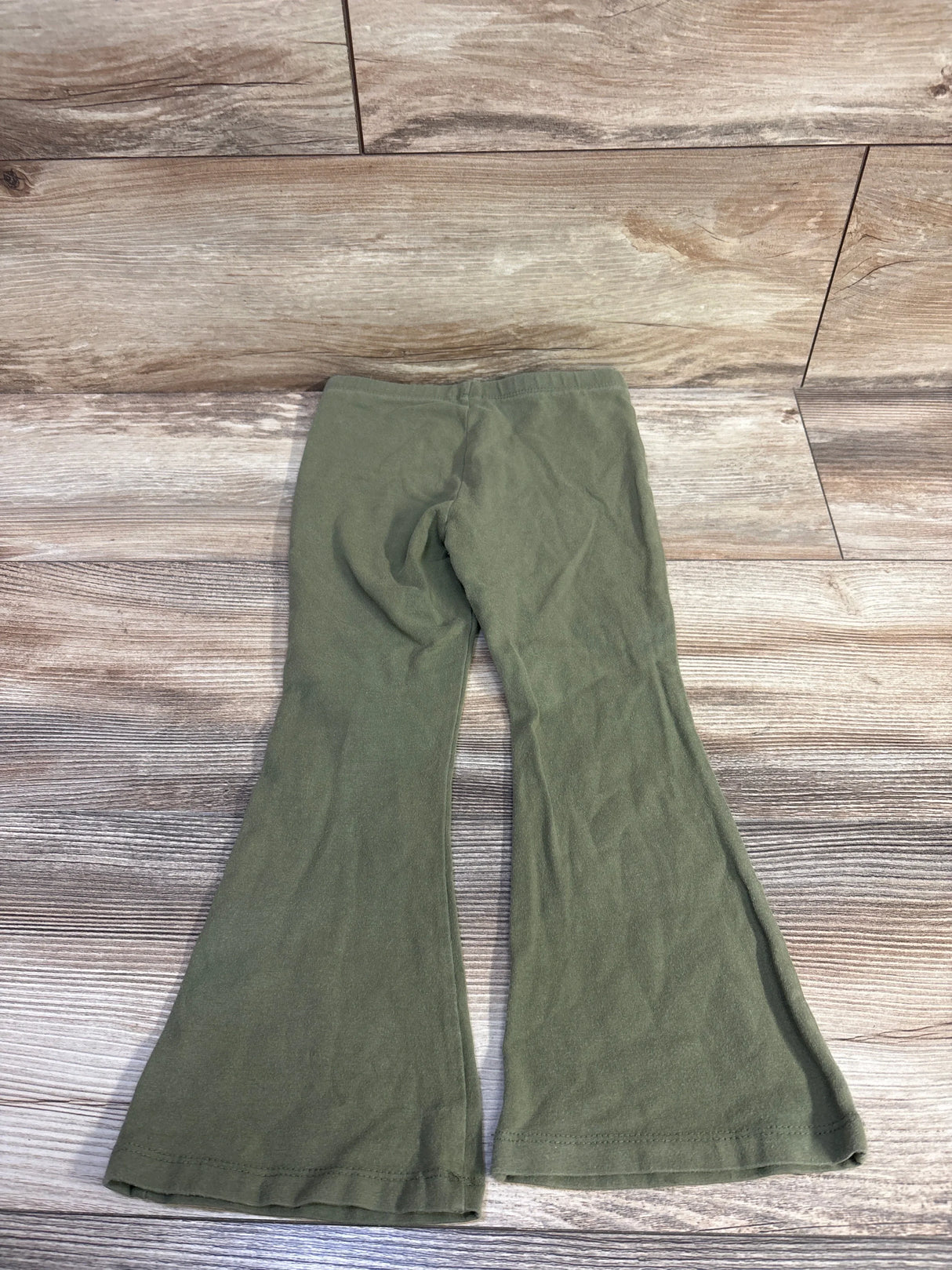 Flat lay of green Cat and Jack toddler flare leggings (size 4T) showing elastic waistband and flared legs on wood-look background