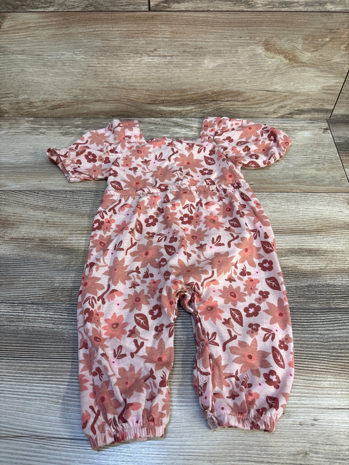 Pink floral baby romper with puff sleeves and snap leg closure on wood background