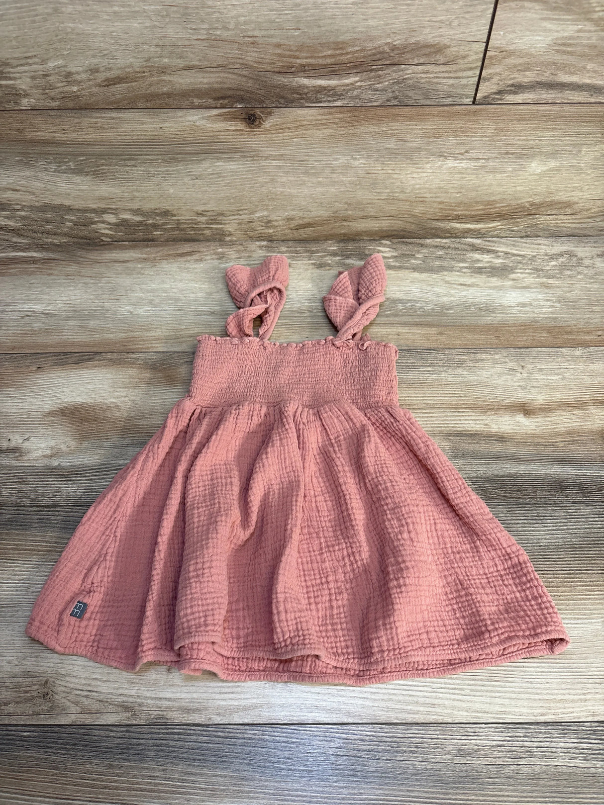 Pink toddler dress with textured fabric and bow straps on wood floor, gently used kids clothing