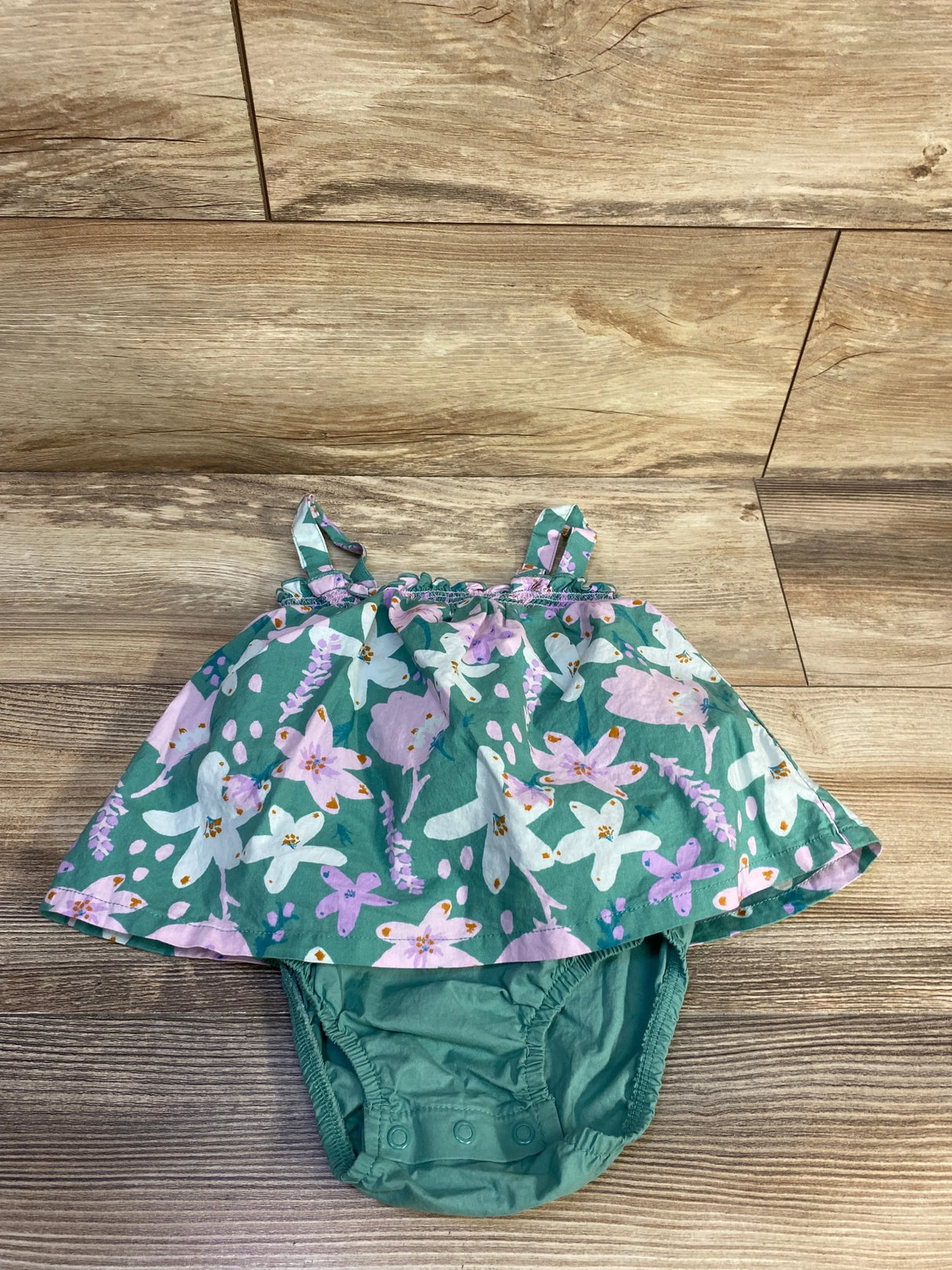 Front view of green floral toddler bodysuit dress with snap closures and ruffled skirt on white background