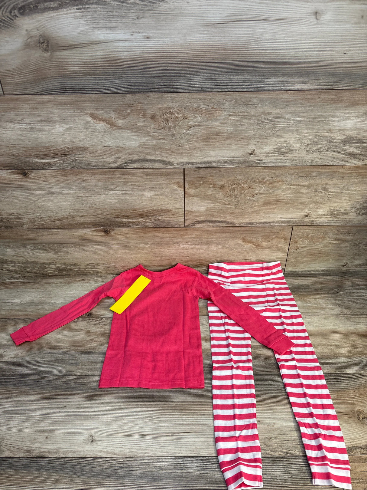 Pink long sleeve toddler pajama set with striped pants on wood background