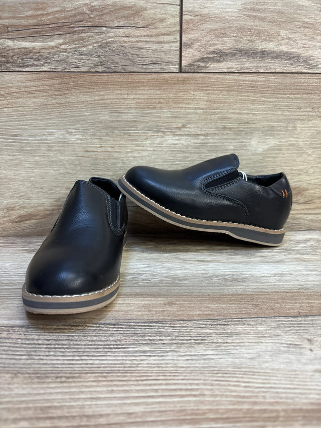 Black kids slip-on dress shoes with tan soles on wood floor