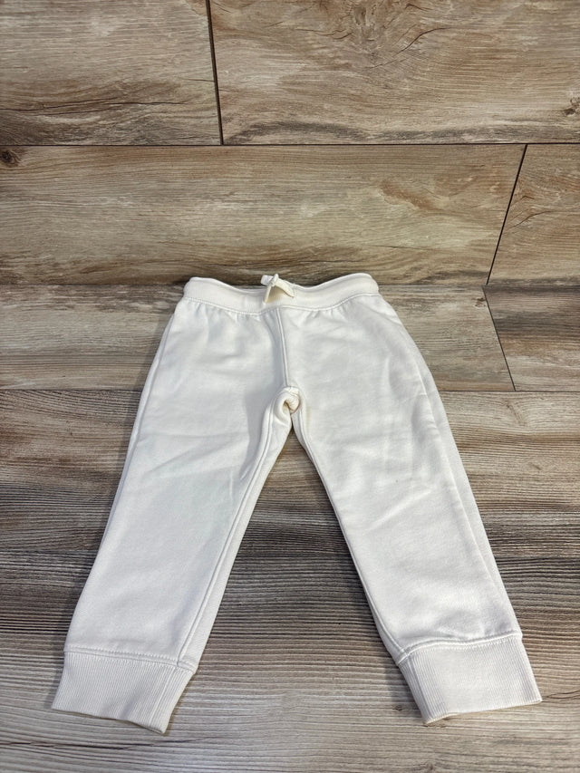 Front flat lay of cream Oshkosh fleece joggers size 3T with ribbed cuffs and drawstring waist on light wood background