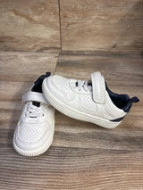 Three-quarter view of Carter's toddler sneakers, white with navy heel, perforated upper, Velcro strap on wood floor
