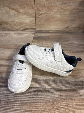 Three-quarter view of Carter's toddler sneakers, white with navy heel, perforated upper, Velcro strap on wood floor