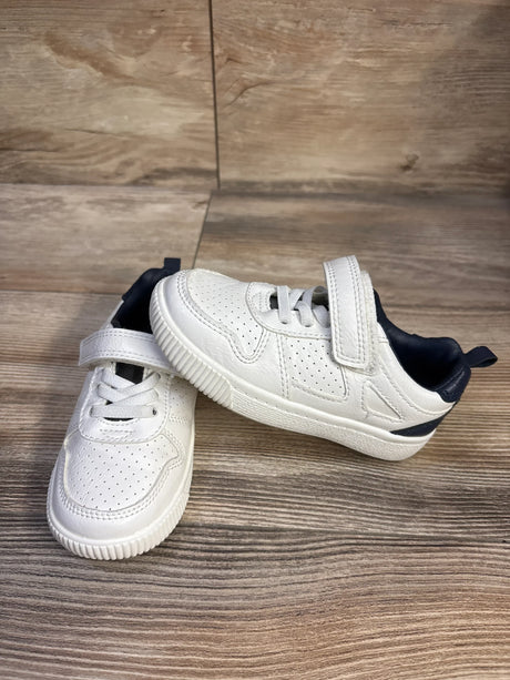 Three-quarter view of Carter's toddler sneakers, white with navy heel, perforated upper, Velcro strap on wood floor