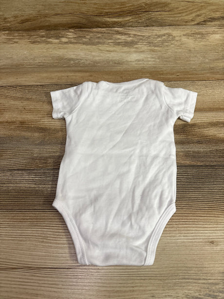 Front view of white In My Lil Sis Era bodysuit showcasing short sleeves and leg openings on a wood-grain background
