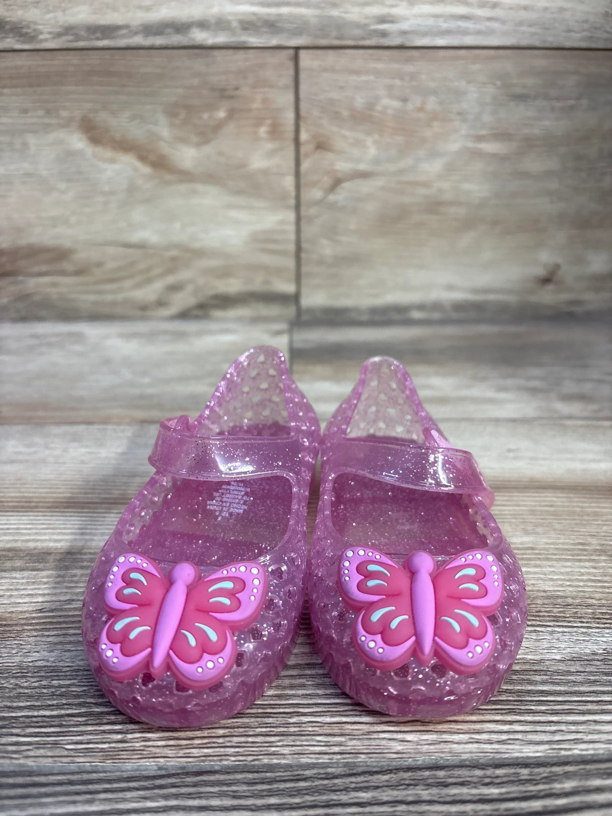 Front view of pink Old Navy jelly Mary Jane flats size 5C showcasing glittered translucent material and butterfly charms on wood floor