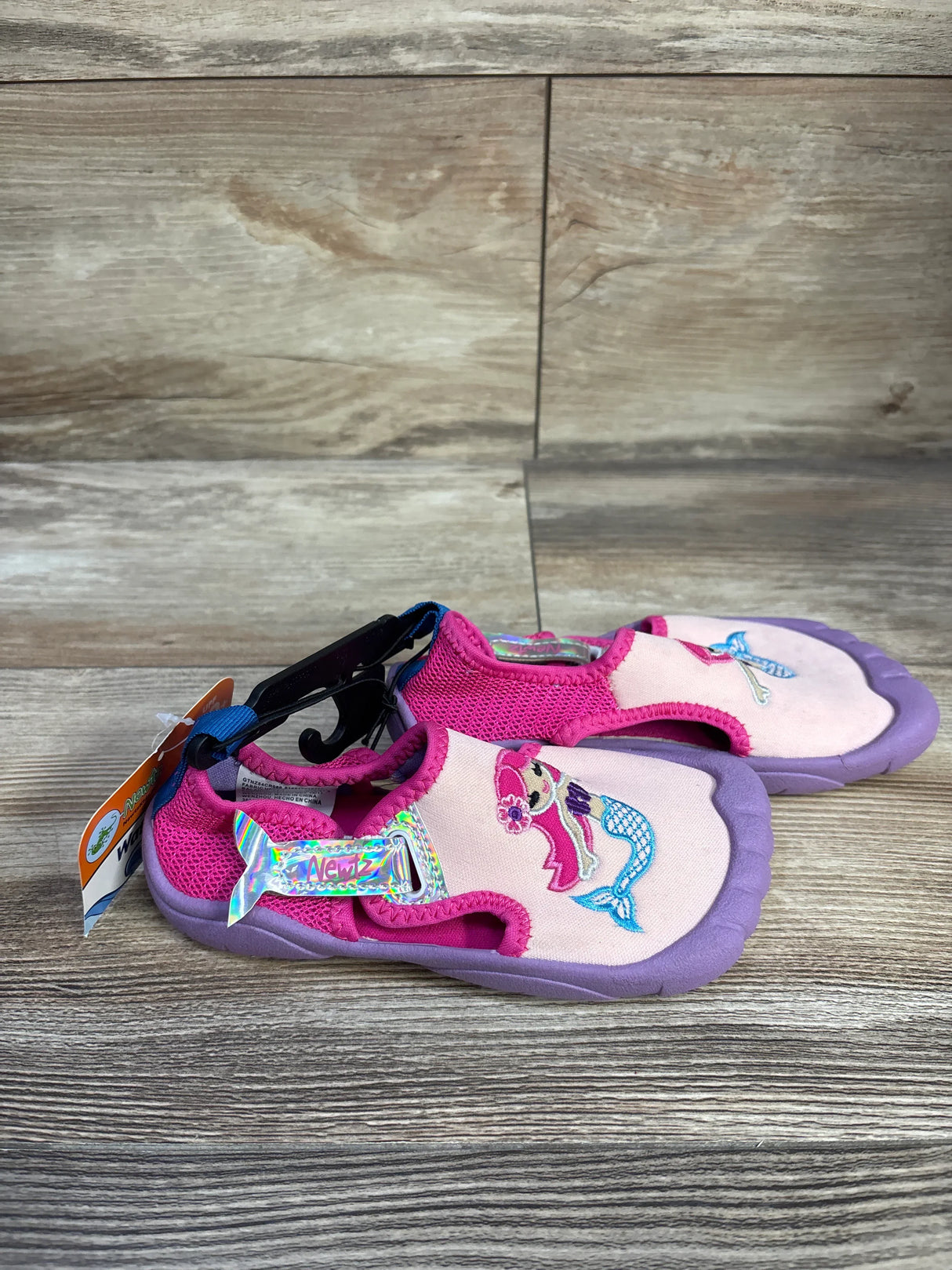 Side view of Newtz mermaid water shoes, pink and purple, embroidered mermaid and holographic tail strap on wood background