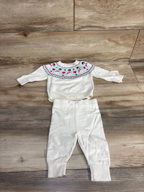 White infant knit sweater and pants set with colorful pattern on chest, laid on wood floor