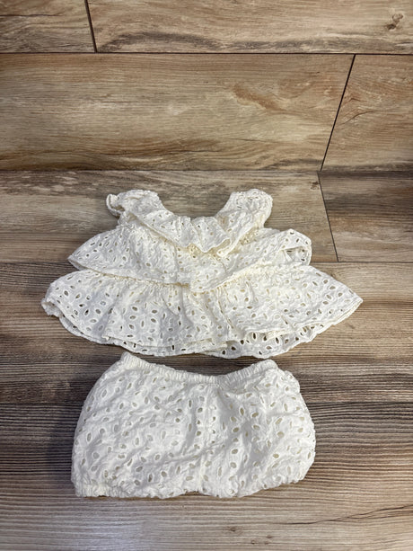 Flat lay of white 2-piece eyelet tiered baby dress with ruffled neckline and matching elastic bloomers, size 6-9 months on wood background