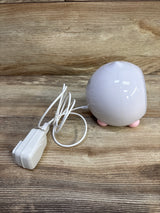 Angled view of LittleHippo Mella Ready To Rise sleep trainer alarm clock showing pink feet and included AC adapter on a wood surface