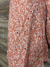 Close up of Isabel maternity blouse fabric, orange with white leaf embroidery and red flower centers on wood background
