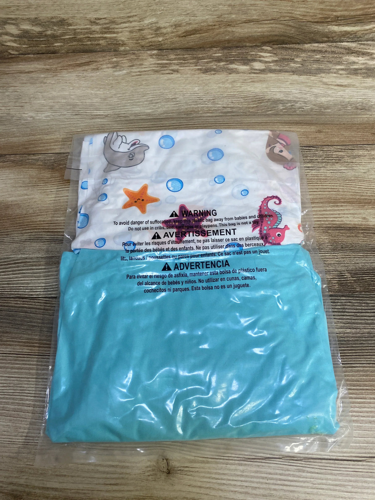 Flat lay of NEW Everyday Kids 2pk Fitted Crib Sheets in teal and sea creature print in original packaging on wood plank floor
