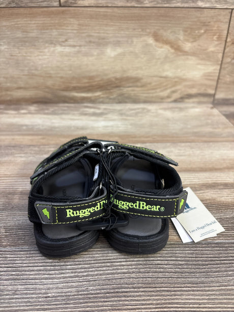 Rear view of Rugged Bear kids' black open-toe sports sandals with branded heel straps and green stitching on wood background