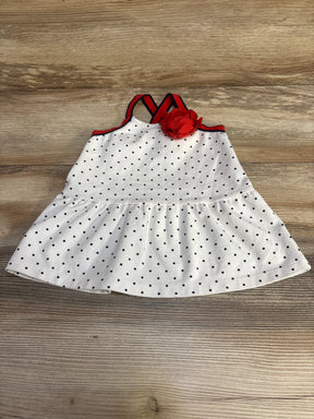 Top down view of white ponte baby dress with black polka dots, red trim and red flower at crossed straps on wooden background