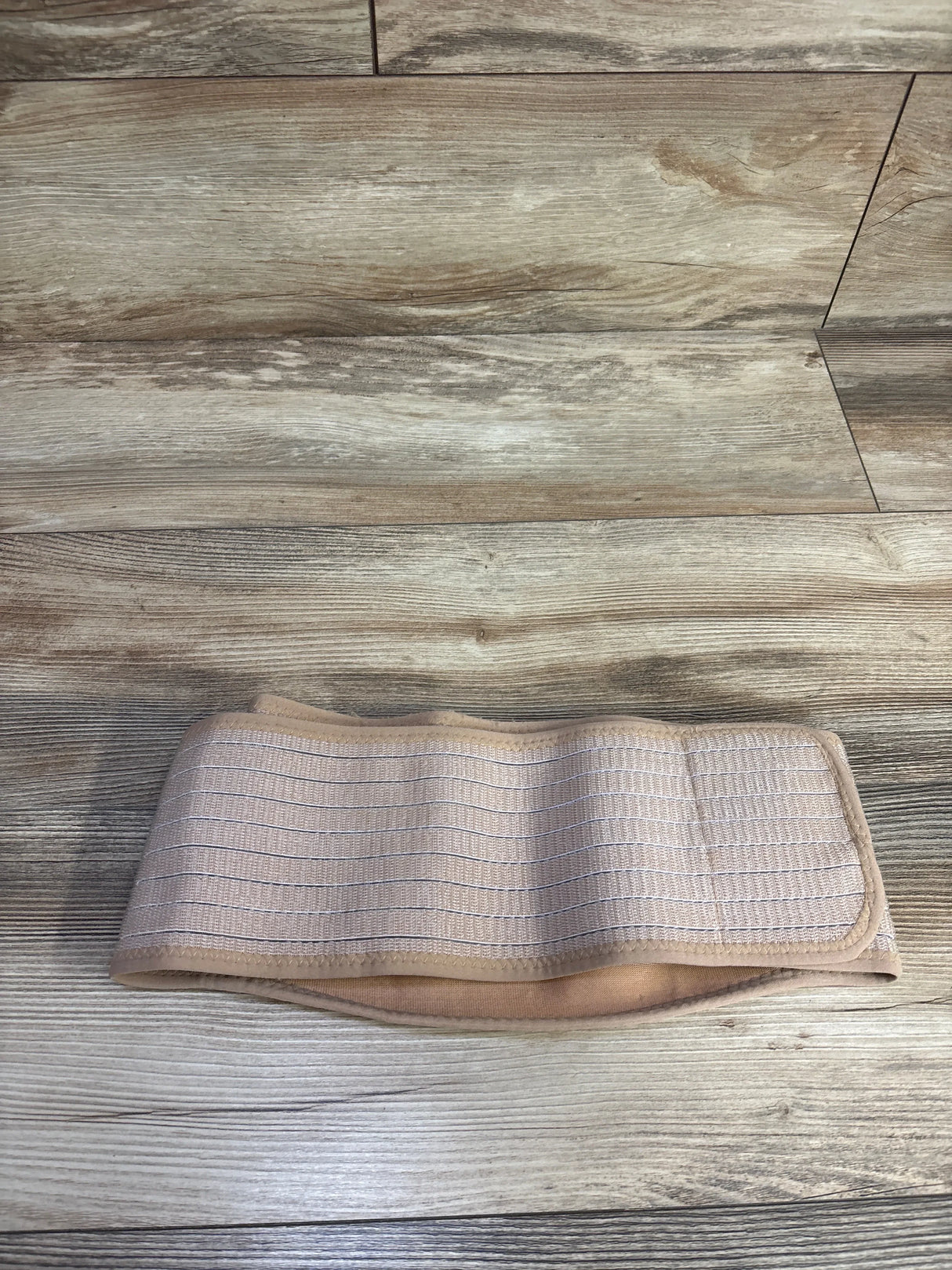 Flat lay of AJ Maternity belly band showing elastic ribbed front and soft padded lining on wood floor