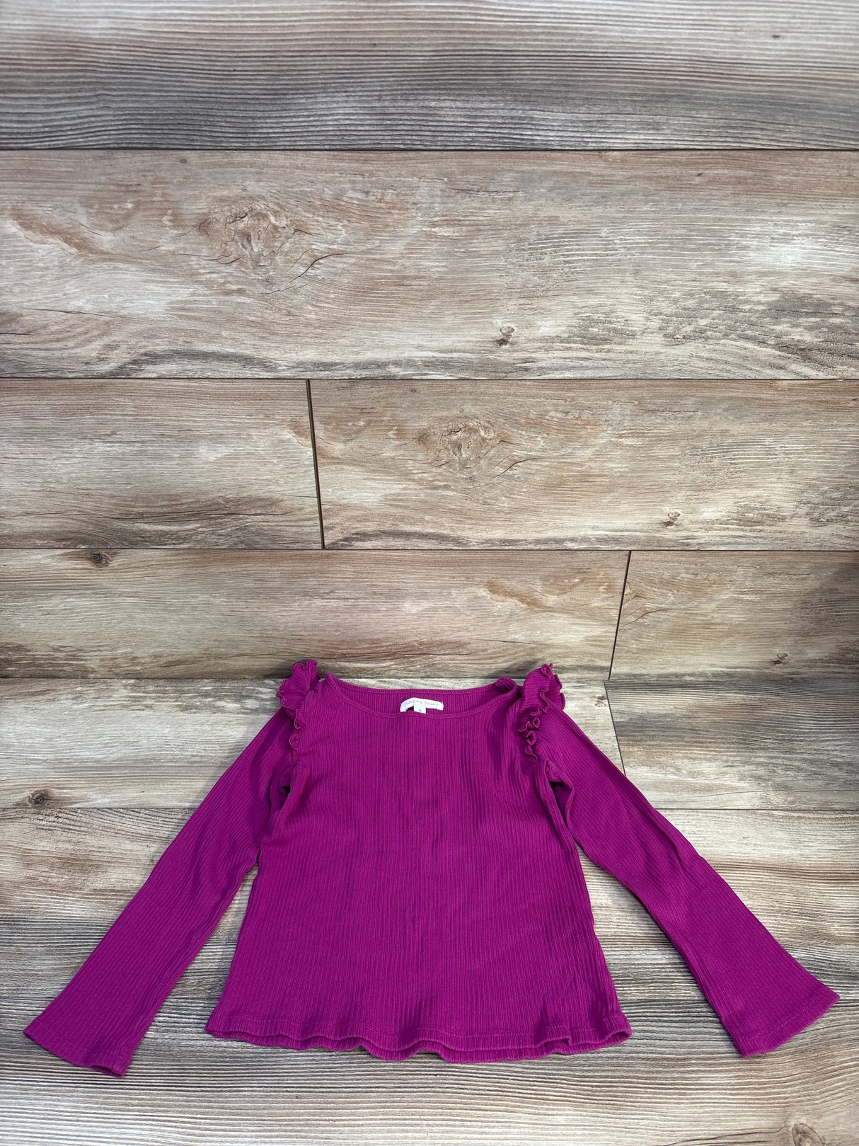 Flat lay of Jumping Beans purple ribbed shirt (5T) showing ruffled shoulders and scalloped hem on wood background