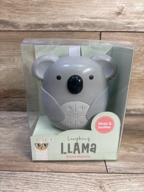 Front view of Laughing Llama koala sound machine in clear retail box showcasing control buttons and fabric speaker panels on a wood background
