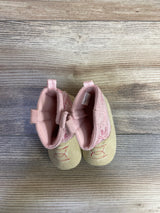 Top-down view of Stepping Stones baby cowgirl crib boots in pink showcasing embroidered cowboy stitching, pull tabs, and soft soles on wood-plank background