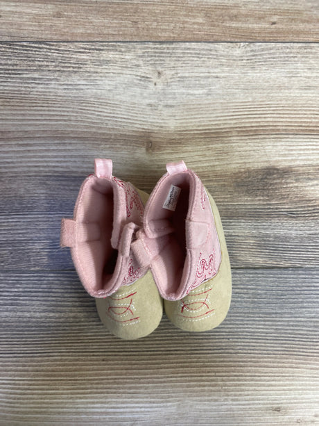 Top-down view of Stepping Stones baby cowgirl crib boots in pink showcasing embroidered cowboy stitching, pull tabs, and soft soles on wood-plank background