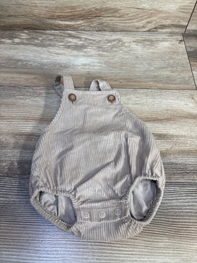 Top-down view of beige corduroy newborn shortalls showing buttoned bib straps and three snap diaper closures on wood floor background