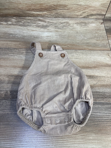 Top-down view of beige corduroy newborn shortalls showing buttoned bib straps and three snap diaper closures on wood floor background