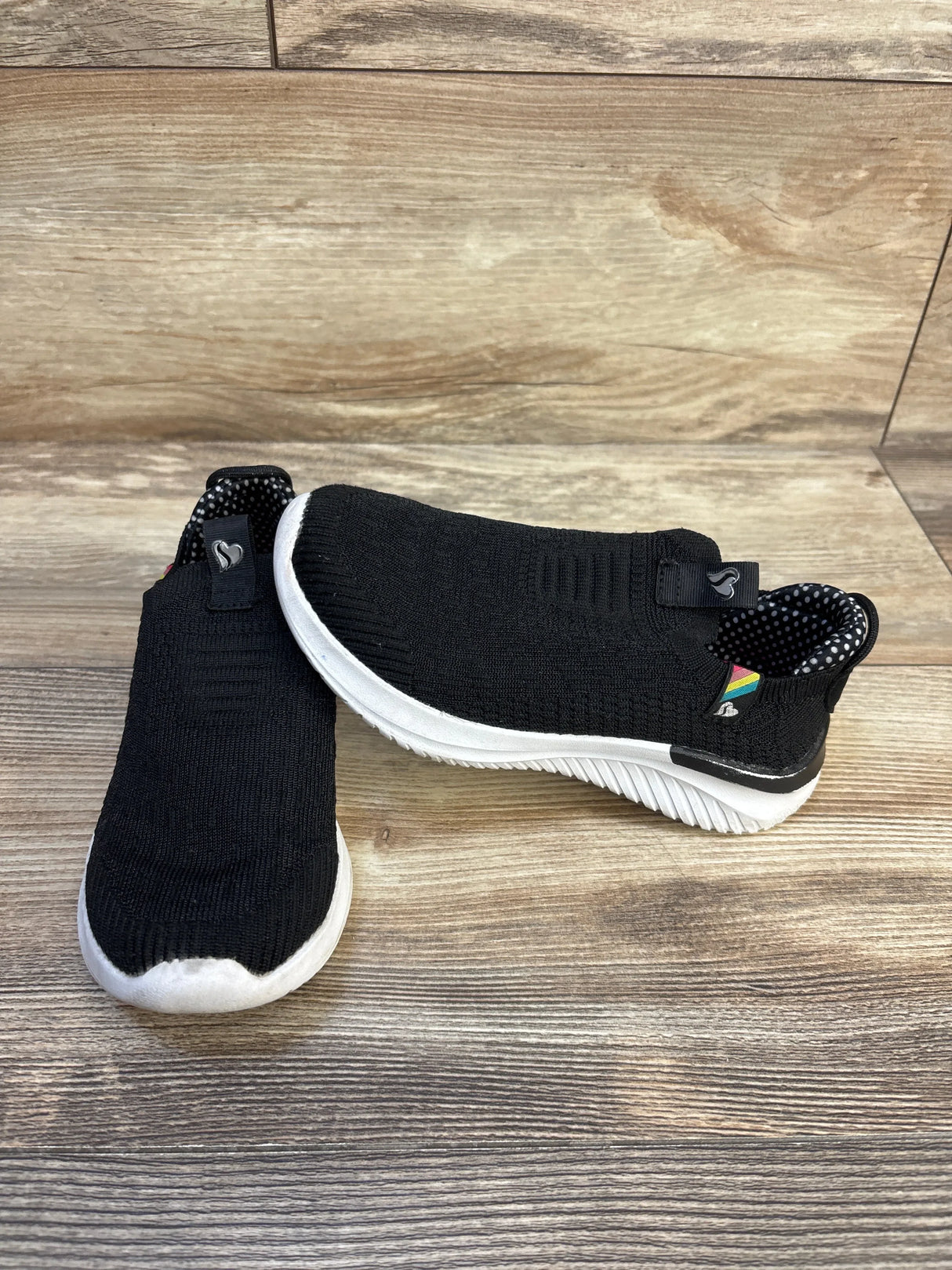 Black knit slip-on kids sneakers with white soles on wood background