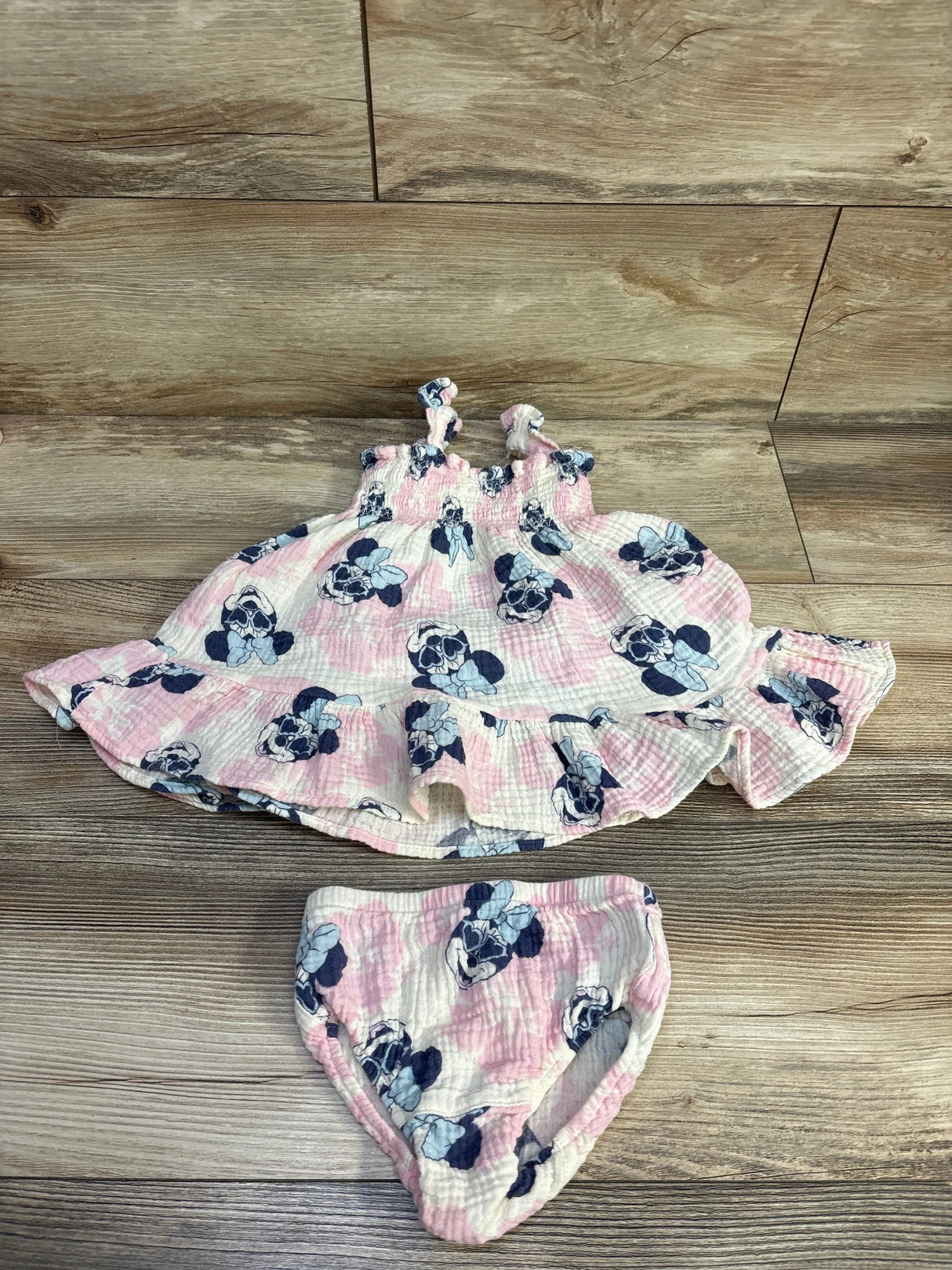 Flat lay of Disney Baby gauze dress and bloomers showing pink and navy Minnie Mouse print on wood background