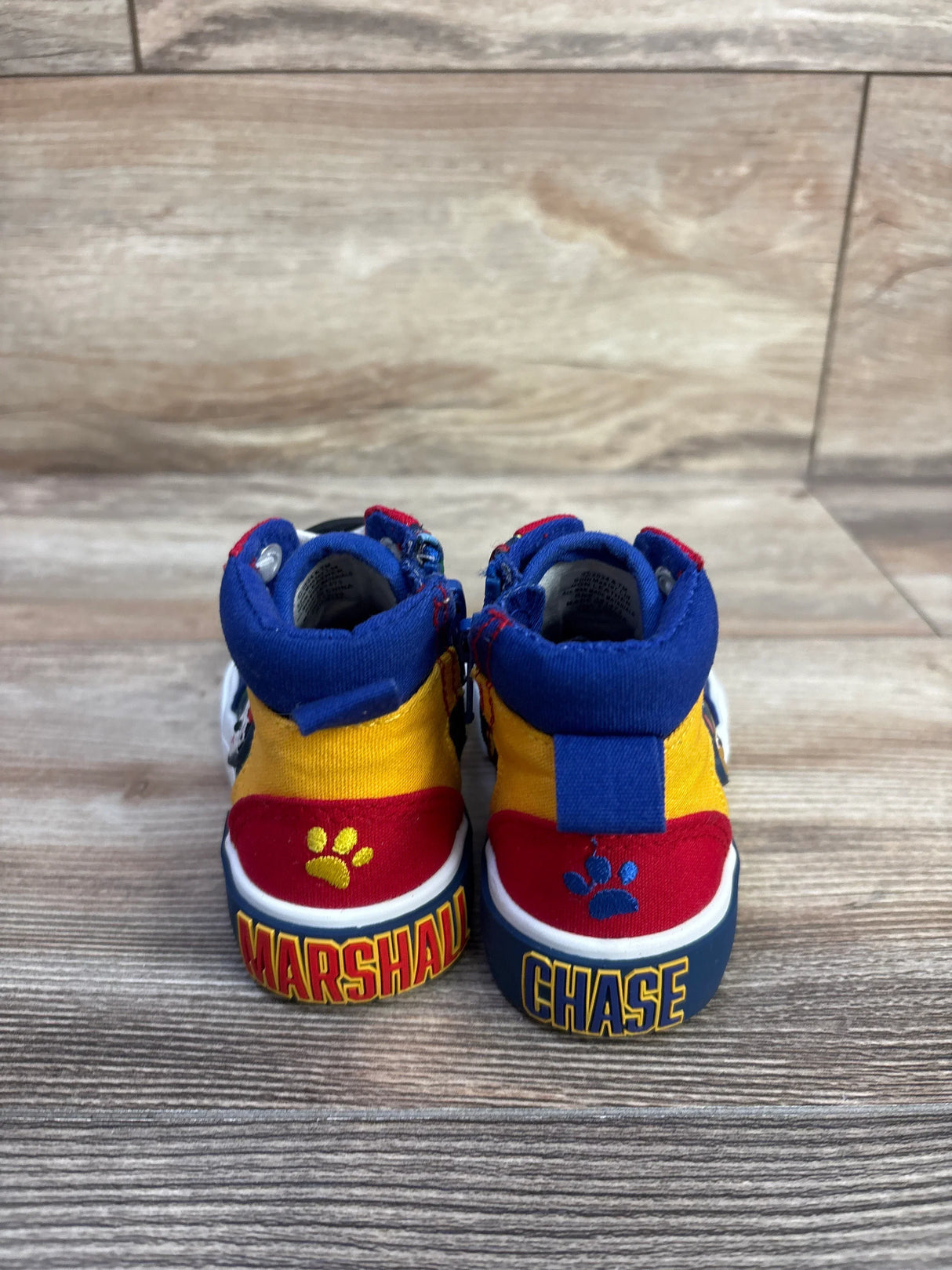 Rear view of toddler high-top Paw Patrol sneakers size 6C with Marshall and Chase on heels and paw-print detail on wood floor