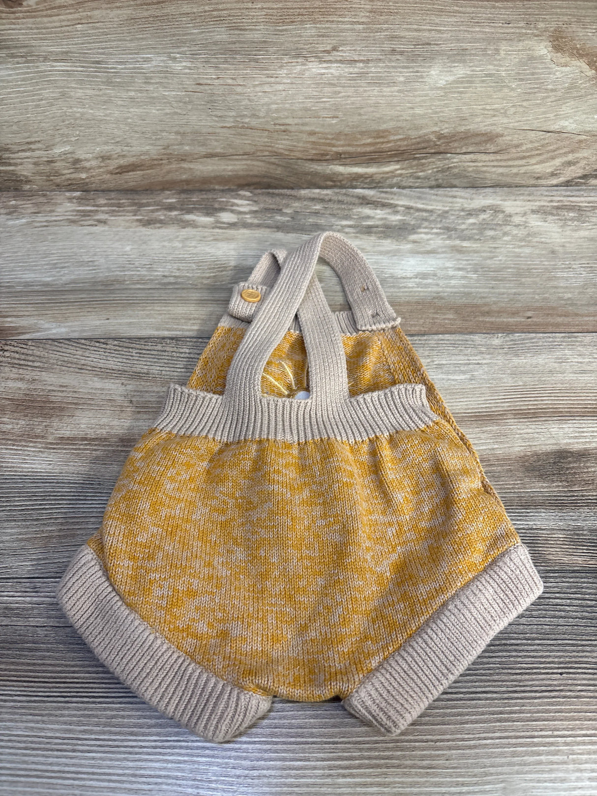 Flat lay of beige and mustard knit baby bubble romper with crossed straps, ribbed trim, and button closure on wood