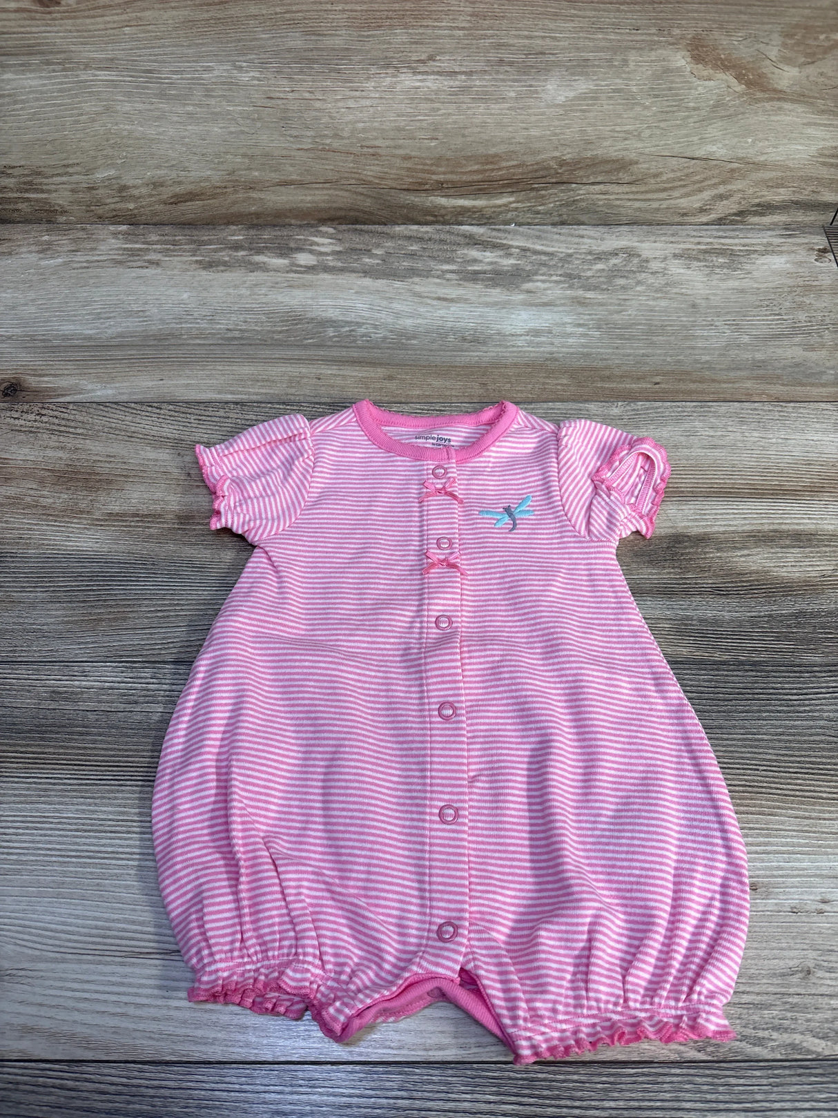 Flat lay of pink striped shortie romper showing front snaps, ruffle sleeves, embroidered bird and elastic legs on wood
