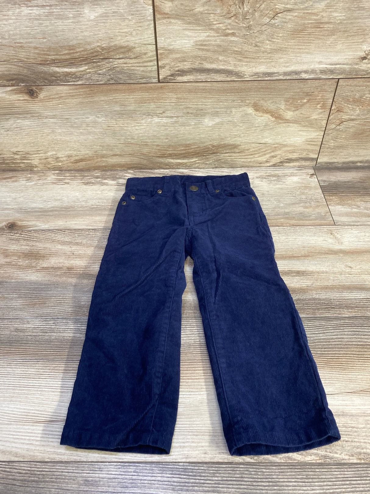 Front view of Janie and Jack navy toddler corduroy pants, size 2T, showing front pockets, button closure on wood floor