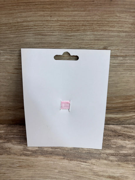 Front view of lollipop applique hair bow on white display card showing small pink ribbon applique against wood background