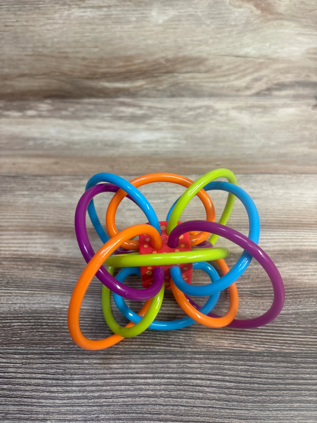 Colorful plastic baby teething toy with interlocking loops on wooden surface