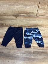Flat-lay of 2-pack newborn pull-on baby pants with elastic waist and cuffed ankles, one solid navy and one blue camouflage on wood background